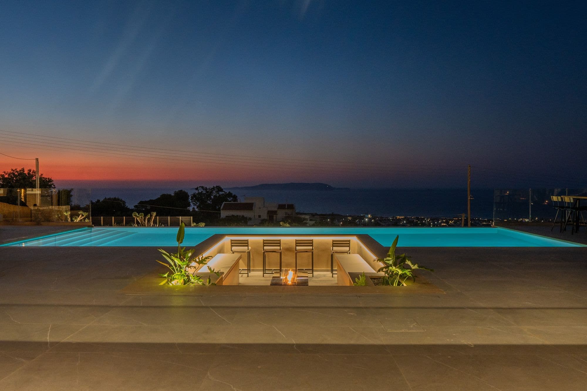 Illuminated pool and sunken lounge at twilight with the last light over the Cretan Sea